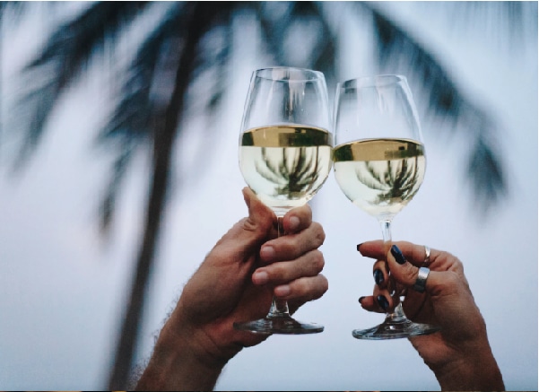 Dos novios durante su boda estilo Las Vegas en el Caribe, brindando con copas de vino blanco en la playa